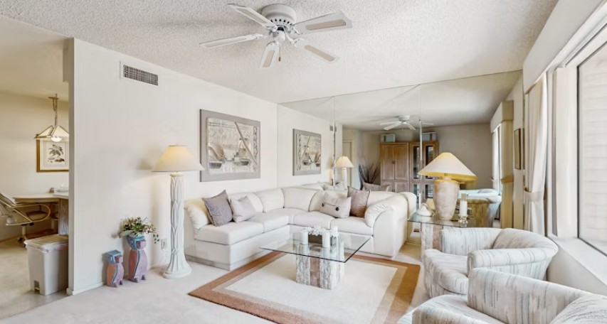 Bright condo living room with sectional sofa, ceiling fan and mirrored wall